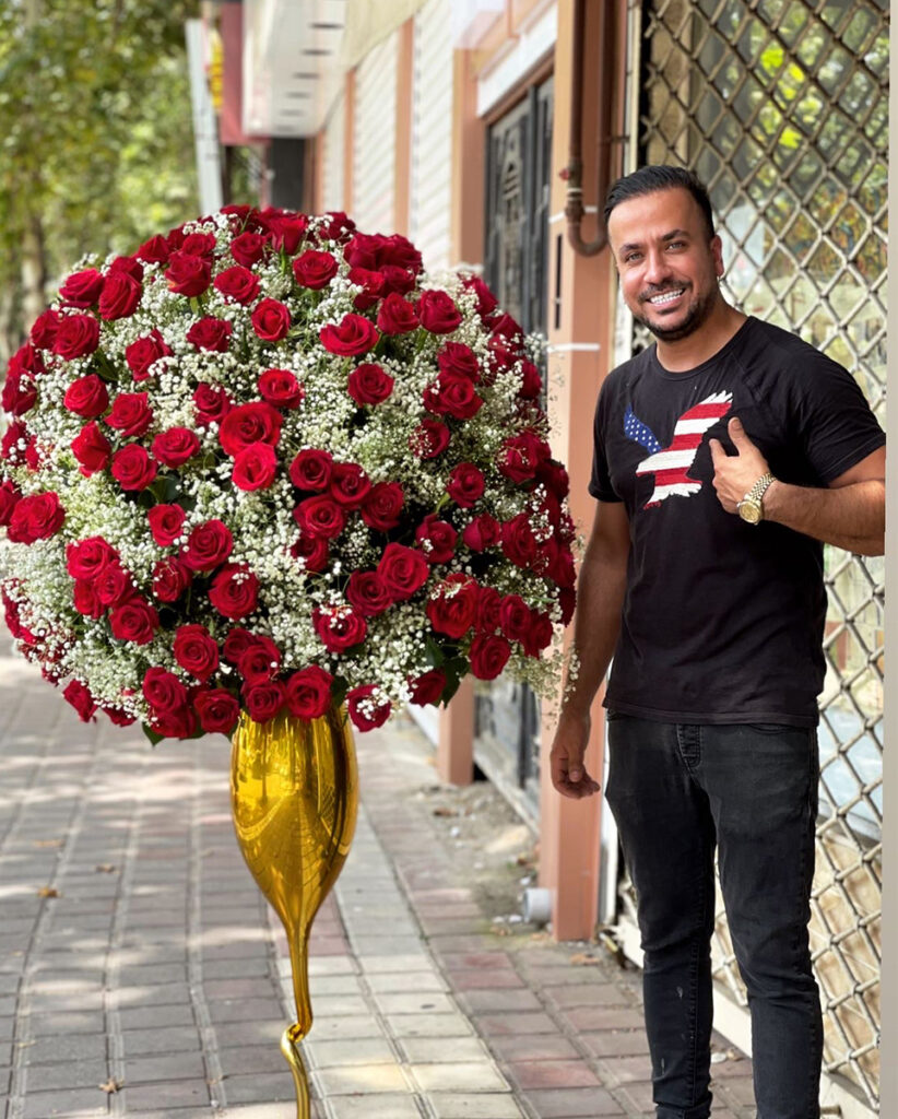 نمایی از میلاد شریفیان با یک دسته گل ایستاده در مقابل گل اکسیژن گلسار رشت