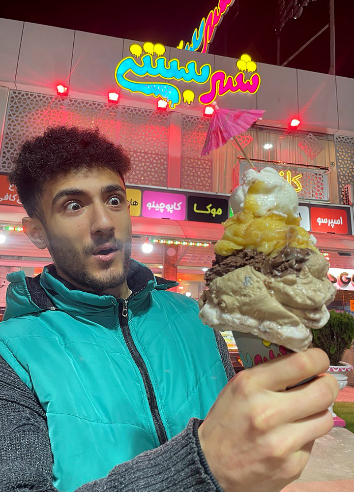 نمایی از امید کاظمی مدیریت شهر بستنی شعبه دوم در شهر خمام که یک قیف پر از بستنی و معجون را در دست دارد و به آن نگاه میکند